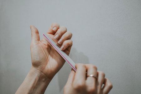 Woman removes nail length with nail file by herself at home. File nails, body hygiene. High quality photoの写真素材
