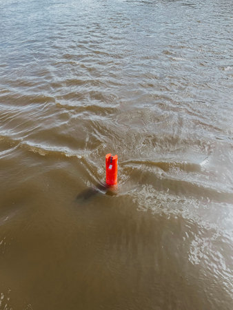 Red freestanding buoy in river with depth in city center of Europe. Strong current and waves. High...