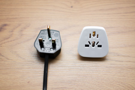 White universal adapter and black cable with UK plug on wooden table, close-up.の写真素材