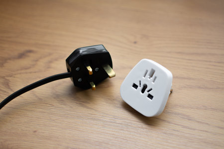 White universal adapter and black cable with UK plug on wooden table, close-up.の写真素材
