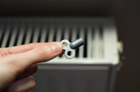 Small metal radiator key placed on a radiator, used to release trapped air from the heating system. High quality photoの写真素材