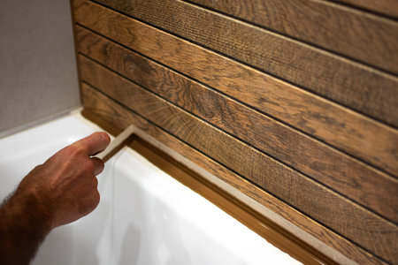 The tiler removes construction tape to finish sealing the grout between the tile and the bathtub, the process of completing construction work. High quality photoの写真素材