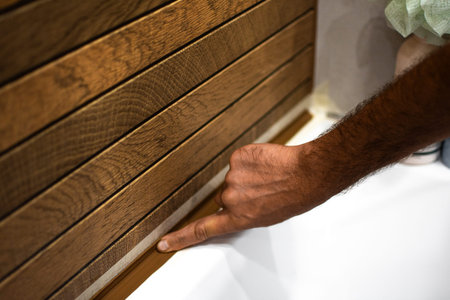 The tiler spreads silicone with fingers to seal between the tile and the bathtub to prevent leaks....