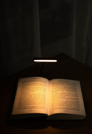 Reading a book at a wooden desk in the evening with the help of a convenient clip-on lamp