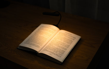 A convenient clip-on reading lamp with color options, placed over a book on the table for reading. Eye protection in the dark and suitable warm light for health. High quality photoの写真素材