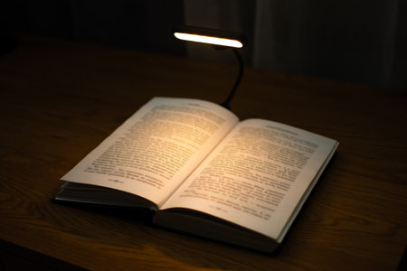 A convenient clip-on reading lamp with color options, placed over a book on the table for reading. Eye protection in the dark and suitable warm light for health. High quality photoの写真素材