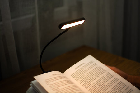 A convenient clip-on reading lamp with color options, placed over a book on the table for reading. Eye protection in the dark and suitable warm light for health. High quality photoの写真素材