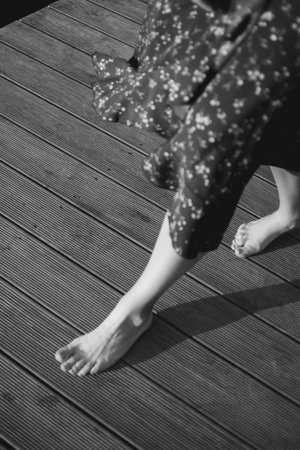 Barefoot woman walking on a wooden pier in summer Estonia, wearing a brown floral dress. Warm sunlight, natural atmosphere, and peaceful European nature.の写真素材