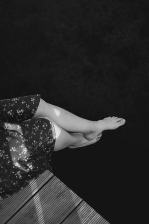 Barefoot woman sitting on a wooden raft above a calm lake in summer Estonia. Her legs hang over the water, surrounded by peaceful nature and warm sunlight.の写真素材