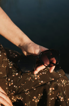 Female hand holding sunglasses near water, summer in Estonia, warm and peaceful atmosphere. High quality photoの写真素材