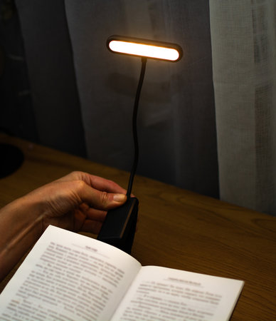 A convenient clip-on reading lamp with color options, placed over a book on the table for reading. Eye protection in the dark and suitable warm light for health. High quality photoの写真素材