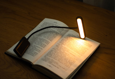 A convenient clip-on reading lamp with color options, placed over a book on the table for reading. Eye protection in the dark and suitable warm light for health. High quality photoの写真素材