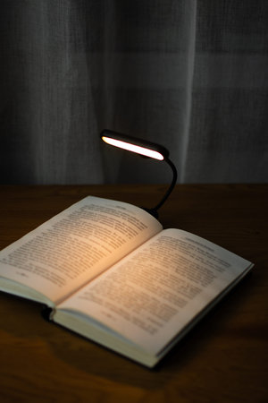 Reading a book at a wooden desk in the evening with the help of a convenient clip-on lamp. Eye...