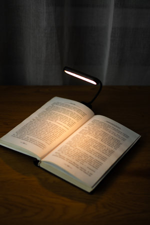 A convenient clip-on reading lamp with color options, placed over a book on the table for reading. Eye protection in the dark and suitable warm light for health. High quality photoの写真素材