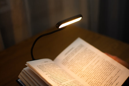 A convenient clip-on reading lamp with color options, placed over a book on the table for reading. Eye protection in the dark and suitable warm light for health. High quality photoの写真素材