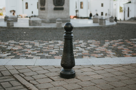 Metal column in close-up on the sidewalk against cobblestone streets in the center of Minsk. The morning sun highlights the texture of the column and the pavement, creating an urban cityscapeの写真素材