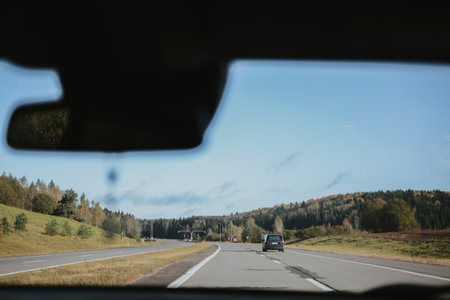 Autumn highway, view through a car windshield with forest and clear sky in the distance.の写真素材
