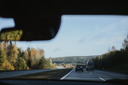 Autumn highway, view through a car windshield with forest and clear sky in the distance.の写真素材