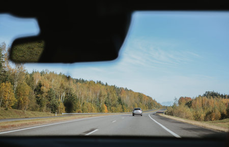Autumn highway, view through a car windshield with forest and clear sky in the distance.