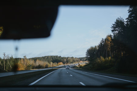 Autumn highway, view through a car windshield with forest and clear sky in the distance.の写真素材