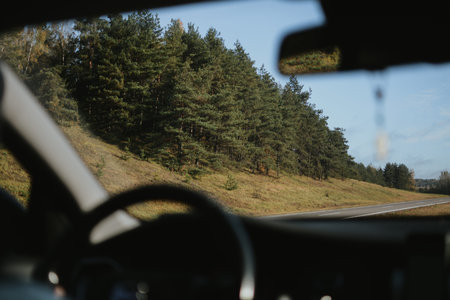 Autumn highway in Belarus, view through a car windshield with forest and clear sky in the distance.
