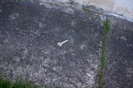 Metal door key lying on asphalt next to grass outdoors. High quality photoの写真素材