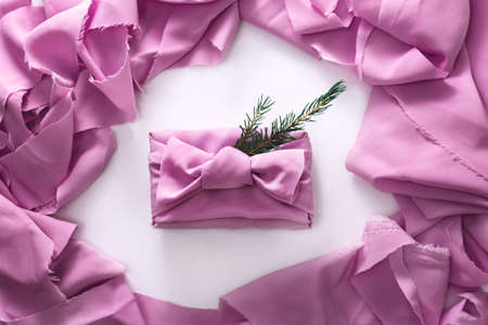 The gift box is wrapped in a beautiful pink cloth surrounded by a frame of waste fabrics. Christmas tree branch on top of a present. Japanese friendly reusable, packaging method. The concept of zero waste. Flat lay composition.の写真素材