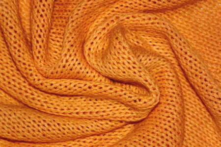 Texture of a warm orange knitted sweater with folds. Pigtails pattern, soft focus. Flat style, close-up.の写真素材