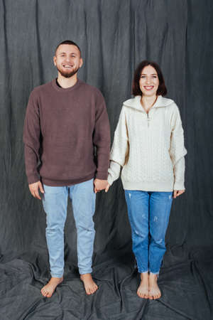 Young and beautiful couple shyly holding hands on a first date. Gray fabric background.They Wear casual jeans and sweaters.の写真素材