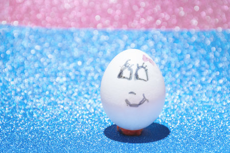 White Easter egg with painted face with a smile on a blue and pink bright background. The concept of the holiday and handicrafts.の写真素材