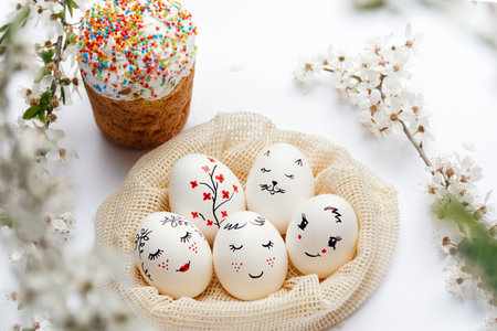 White Easter eggs in a mesh eco-bag with beautiful painted faces and a delicious Easter cake with...
