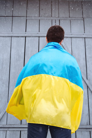 The man is wearing the state flag of Ukraine on his shoulder and is standing with his back to the camera outdoors in snowy weather. Ukrainian flag, patriotism. Independence Flag Day of Ukraine.の写真素材