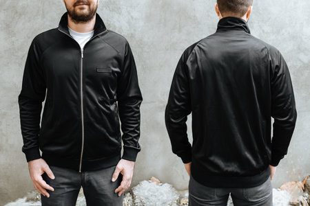 Young man with a beard in a black sports jacket. Front and rear view on a background of light gray concrete wall. Design and layout of men's uniforms for printing.の写真素材