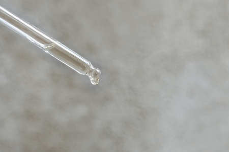 Transparent glass pipette with essential oil or serum on a light gray concrete background. A drop of cosmetic oil falls. copyspace.の写真素材