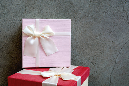 Front view of two beautiful gift boxes with satin ribbon on natural concrete wall background. Pink...