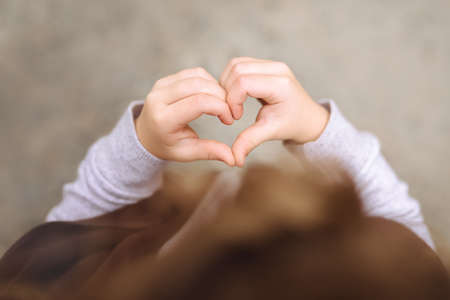 Close up of baby making heart shape with his hands on gray background. A sign of love and happinessの写真素材