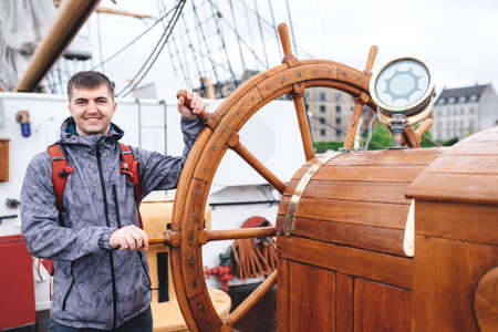 A young guy traveler stands at the helm of a ship in the sea. Smiling happy man enjoying summer vacation. Adventures, holidays, thirst for the new. Soft focus.の写真素材