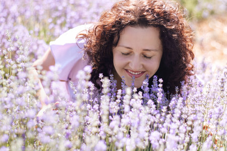 Romantic close-up portrait of curly girl enjoying scent of lavender, closed her eyes in field on sunny day. Girl walks pink field of flowers. Digital detox, pleasure ofslow life. Soft Selective focusの写真素材