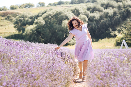 Soft selective focus girl in purple dress walks on lavender field and enjoys the aroma of pink flowers and beauty on sunny day. Trendy color of 2022 Very peri. Digital detox pleasure of slow life.の写真素材