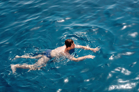 The guy swims in the blue calm sea water or ocean. Gentle sun glare on the surface. The concept of...