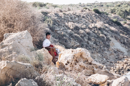 Rocky landscape, Cape Greco Peninsula Park, Cyprus. Soft selective focus man sitting on bench with backpack on hot sunny day. Tourist in white linen shirt, enjoys silence of holiday. Digital detox.の写真素材