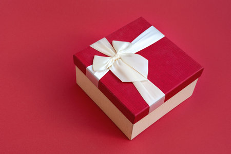 Top view of beautiful red gift box with satin light ribbon on red background. A gift for Christmas, New Year or a romantic Valentines Day. Copy space for text.の写真素材