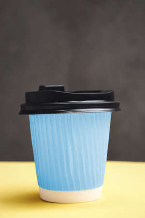 Blue paper cup with takeaway coffee. Container on a yellow and dark gray background. Concept of adding taste and color to life. Copy Space for textの写真素材