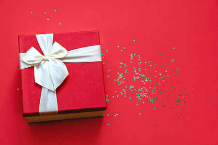 Soft focus and top view on beautiful red gift box with satin light ribbon on red background. Green Glitter stars are shining on the table. Gift for Christmas and New Year. Copy space for text.の写真素材