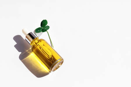 Dropper glass Bottle Mock-Up with metal lid, essential oil and leaf of healing clover lying on white background. Serum, cosmetics, massage oil. Natural light, beautiful orange shadows. Copy spaceの写真素材