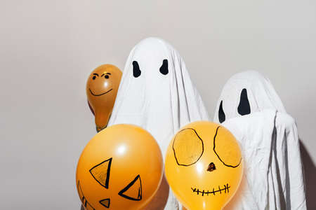 Happy Halloween, Autumn. Children dressed up in white ghost costumes and painted orange balloons. Different emotions of joy, anger, laughter. Costumes made by hand.Festive decoration, party concept.の写真素材