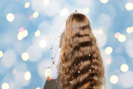 Rear view of a girl with long wavy flowing hair on a bright shimmering blue and yellow background. A crown and garlands of snowflakes for a child. Merry Christmas and Happy New Year. Copy space.の写真素材