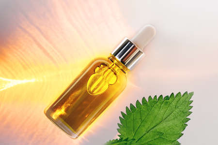 Close-up mockup of glass dropper bottle with metal cap and yellow nettle essential oil on a background with an abstract fire light, shadow pattern. Eco cream, serum, cosmetics, massage oil. Copy spaceの写真素材