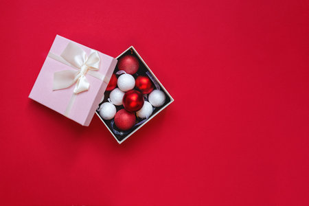 Beautiful red and white Christmas decorations in a pink open gift box on red background. Top view on...
