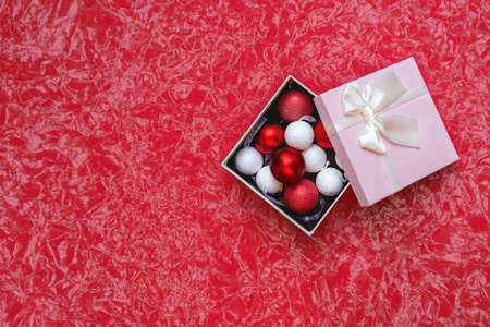 Red and white Christmas decorations in a pink open gift box on a red abstract background. Top view of round toys. Concept of Christmas, preparation for the holidays. Copy space. Soft selective focusの写真素材